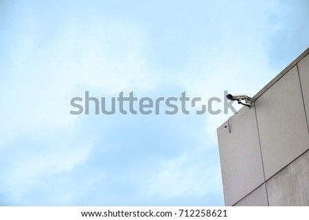 Security camera on side of a building and blue sky background.