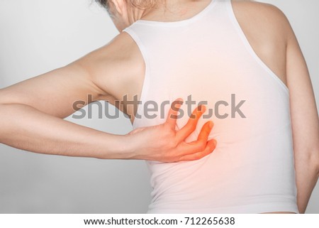 woman with back pain. Female holding hand to spot of back. Concept photo with read spot indicating location of the pain.
