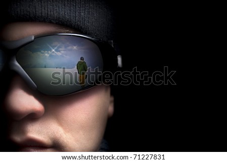 Portrait of a young man close up. In the glasses reflection the mountains and snowboarders