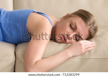Beautiful young woman sleeping on couch, pretty tired girl lying asleep on sofa, stressed lady taking nap at home passed out after sleepless night, teenager dozing in daytime, head shot portrait Royalty-Free Stock Photo #712283299