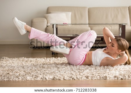 Young fitness girl doing easy intensive bicycle crunches exercise at home lying on floor, sporty woman training abdominal oblique core muscles for burning fat, flat abdomen or slender legs, side view Royalty-Free Stock Photo #712283338