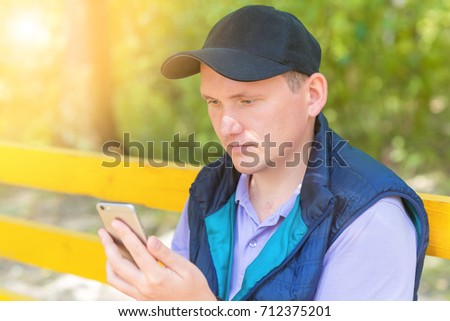 A man sits in a park on a bench and looks into the phone