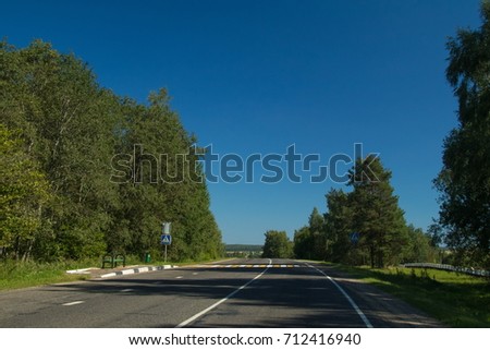 A wide road, green trees and a dark sky with gray clouds