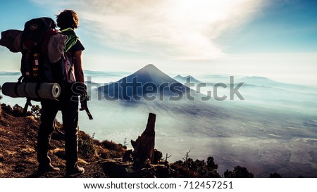 Rear view of traveler guy with backpack looking amazing view of Guatemala mountains. Pick of Volcàn de Agua with one person enjoying the beautiful panorama. Wanderlust vacation concept with adventure 