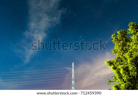 High voltage electric tower in the starry night with tree in foreground