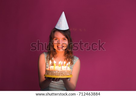 Portrait of joyful girl holding birthday cake and looking at camera at studio