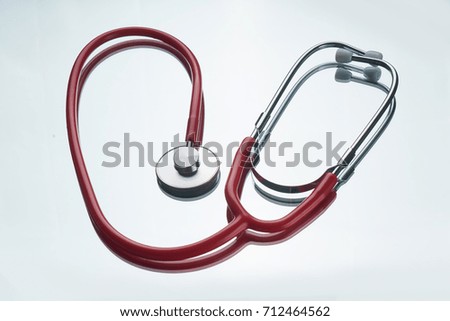 Red color stethoscope with reflection on glossy background.