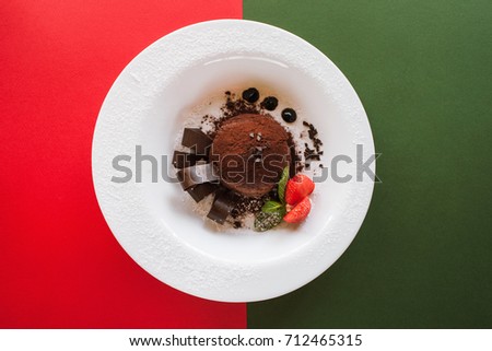 Chocolate fondant on colorful background of red and green. Delicious dessert with decoration from strawberry and mint serving in restaurant, top view with free space