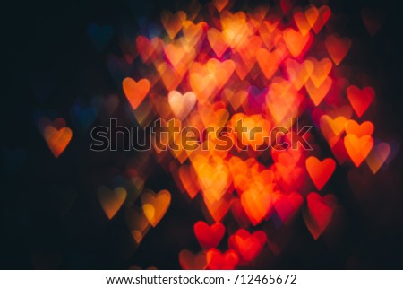Abstract background of colorful hearts on black. Bokeh of defocused glitters, blurred red and orange symbols of love. Festive wallpaper of holidays and celebrations, St. Valentine's day