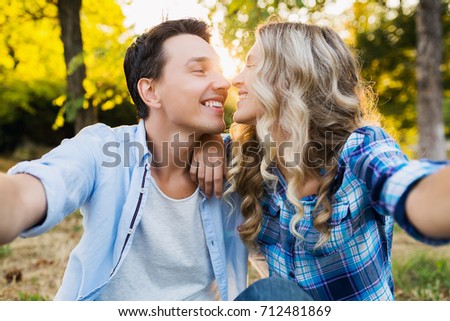 young beautiful couple sitting in park, smiling, happy friends, traveling together, casual denim outfit, summer style, making selfie photo, kissing, romantic mood