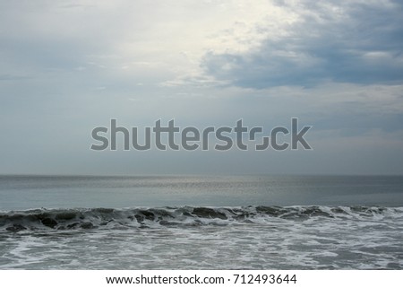Warm light penetrates the cloud cover reflecting off of a serene ocean. A small swell in the foreground makes a slight diagonal across the picture plane.