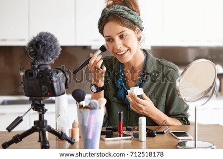Beautiful female advertising cosmetics, making photos with camera for well known magazine while trying new kind of powder. Young woman earning much money from creating her personal cosmetic website