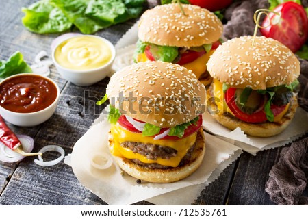 A double burger with a meat cutlet and vegetables is served with cheese sauce and ketchup. Delicious fresh homemade double cheeseburger on a wooden kitchen table. Street food, fast food. Royalty-Free Stock Photo #712535761