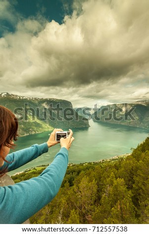 Tourism vacation and travel. Woman tourist taking photo with camera, enjoying Aurland fjord view from Stegastein viewpoint, Norway Scandinavia.