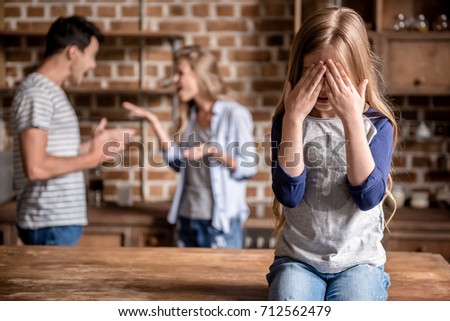 Little girl is crying while her parents are arguing in the background in kitchen Royalty-Free Stock Photo #712562479