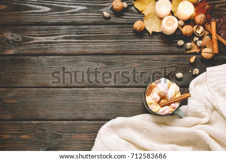 Autumn frame made of dried fall leaves, mug of cocoa with marshmellows, nuts, cinnamon, plaid, apples. Top view on brown wood background