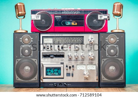 Retro outdated HI FI stereo cassette boom box system, red radio tape recorder from 80s and golden microphones on table front aquamarine background. Vintage instagram  old style filtered photo
