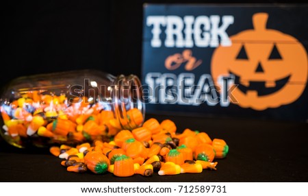 A glass jar has tumbled and spilled some of its candy corn on a table.