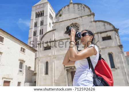 A beautiful tourist woman photographer takes a picture in the city on the background of the architecture.