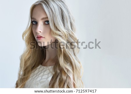 Blonde fashion  girl with long  and   shiny curly hair .  Beautiful  fashion model   with wavy hairstyle .Hair styling tousled waves