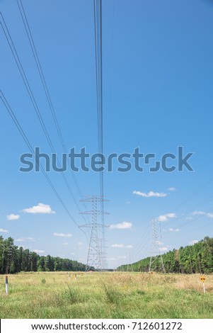 Parallel rows of transmission towers (power tower, electricity pylon, steel lattice tower) cloud blue sky in Houston, Texas, US. Texture high voltage pillar, overhead power line, industrial background