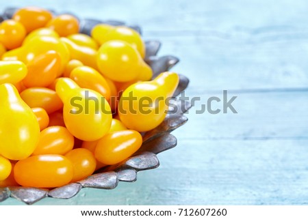 Bowl with datterino cherry tomatoes from the yellow pear variety on a light blue wooden background with copy space