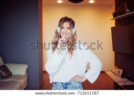 Young pretty girl in headphones with the phone. Listening to music, dancing and singing, indoors