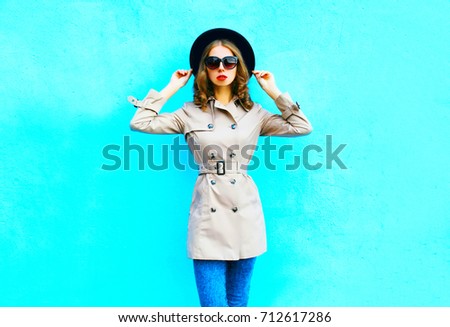 Fashion woman posing wearing a coat and black round hat on a blue background
