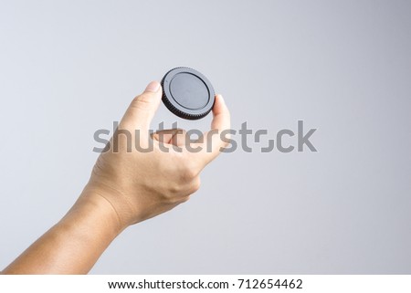 Hand holding lens or camera cap on white background