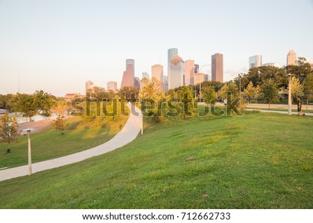Downtown Houston at sunset from Eleanor Tinsley Park, grassy green park lawn, curved pathway with people walking, biking, exercising and modern skylines in background. The most populous city in Texas