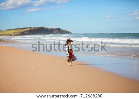 Boy in fancy pirate dress walking on ocean coast, blue sky.