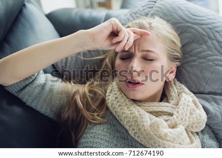 Young woman is laying down on the coach and holding her head  Royalty-Free Stock Photo #712674190