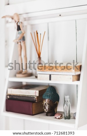 White wooden shelf with different old books and statue of Buddha. Cozy light interior rustic style