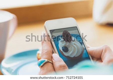 Woman takes a picture of cup with coffee and a cupcake on the plate, soft focus background