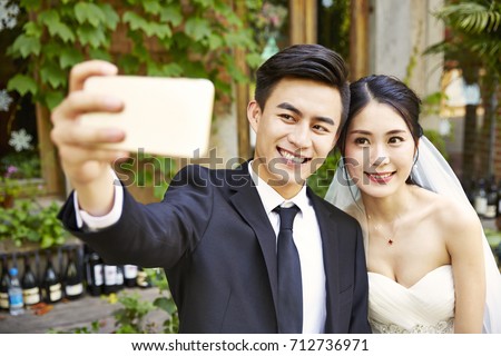 young asian bride and groom taking a selfie using cellphone.