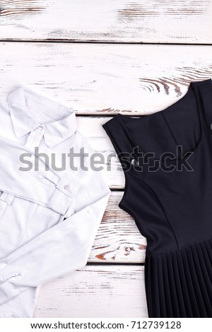 White blouse and black dress for school girl. Girls pretty white shirt and black pleated dress on wooden background. Little girls school uniform on sale.