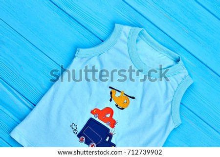 Baby-boy sleeveless cotton t-shirt. Turquoise organic cartoon t-shirt for toddler boys, blue wooden background.