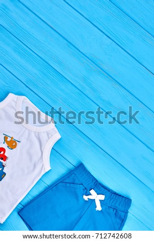 Baby boy summer casual clothes. White t-shirt and blue shorts for little boy on wooden background, copy space.
