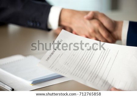 Close up photo of employment agreement document in hand of hiring manager shaking hand of job candidate. Employer offering work contract to applicant, successful interview, positive hiring decision 