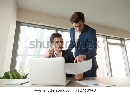 Two coworkers in business suits working together on project documentation in office. Boss giving instructions to employee or assistant. Millennial architects or realtors discussing apartments plan  Royalty-Free Stock Photo #712768948