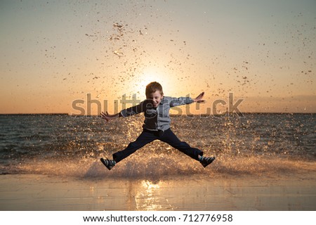 funny little boy jumping against the background of huge waves at beautiful sea sunset