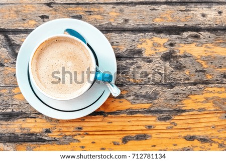 An overhead photo of cup of coffee with milk on a rustic wooden board table, outdoors, with copy space