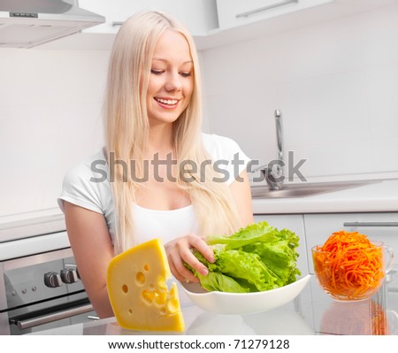 beautiful young blond woman with salad, cheese and carrot in the kitchen at home