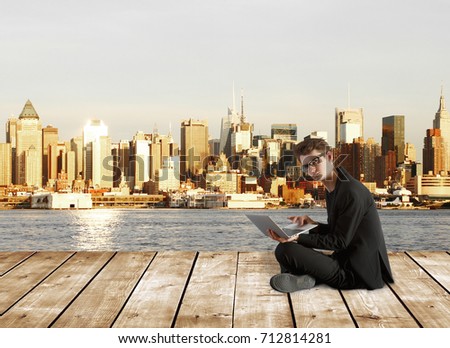 Confused businessman with laptop sitting on wooden pier with city view. Research concept 