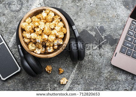 Gray grunge working stone table with laptop, headphones, wooden bowl with caramel popcorn. Modern youth grunge trends. Top View