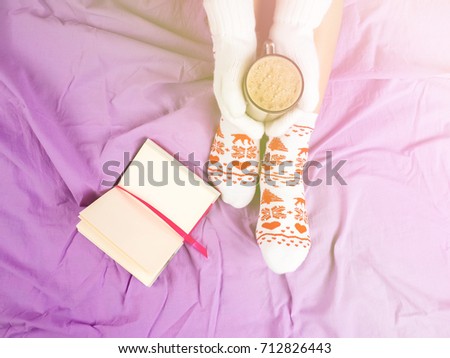Soft photo of woman on the bed with notebook, cup of coffee, top view point.Female legs in warm woolen socks.