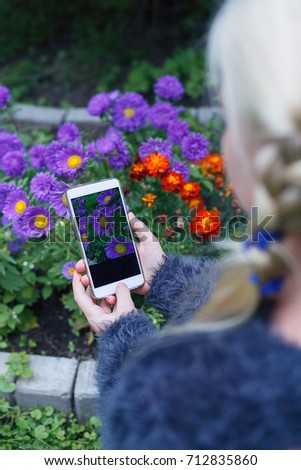 Mobile phone in the hands of a teenage girl on the background of beautiful flowers/teenage girl uses her mobile phone outdoors for photographing flowers