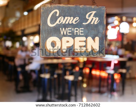 A business vintage sign that says 'Come in We're Open' on Cafe / Restaurant window. Image of abstract blur restaurant with people. Restaurant with customer for background usage