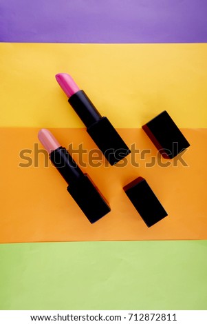 A variety of lipstick make up arranged on a bright colourful background.