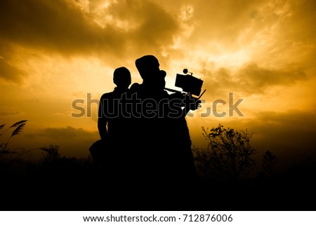 Silhouette figures of a group of people on top of a hill playing drone with dramatic sky / cloud as background